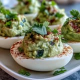 Creamy guacamole-stuffed deviled eggs with fresh avocado, lime, and cilantro for a zesty appetizer.  
