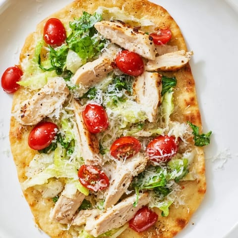 Warm Chicken Caesar Flatbread fresh from the oven, garnished with cherry tomatoes and freshly ground black pepper for a light lunch.