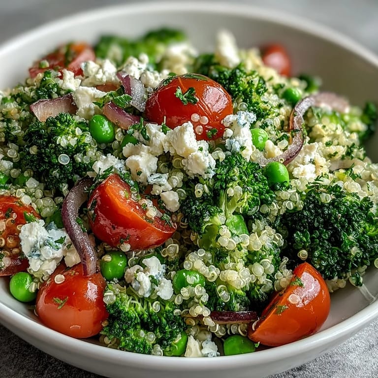 Colorful grain bowl featuring tender quinoa, steamed broccoli, sweet peas, and tangy feta, garnished with parsley and cherry tomatoes.  