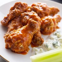 Crispy Buffalo wings coated in spicy red sauce, ready to be enjoyed with celery sticks.