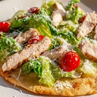Golden-brown flatbread topped with juicy grilled chicken slices, crisp romaine lettuce, and creamy Caesar dressing with parmesan.
