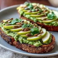 Vibrant avocado and green apple breakfast toast topped with crunchy pumpkin seeds and fresh herbs.  